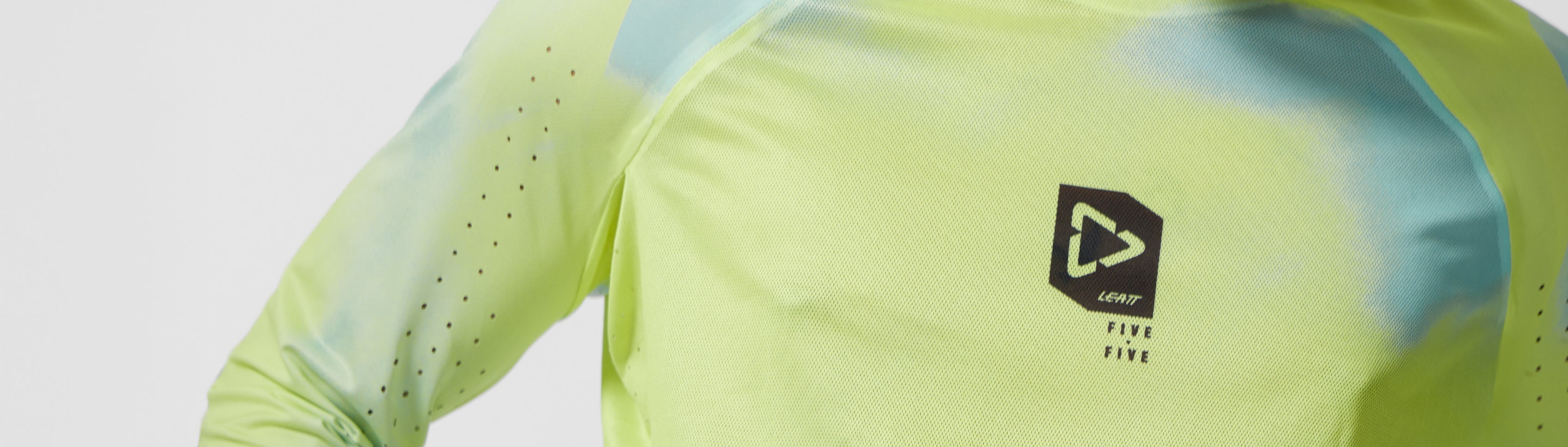 Close-up of a person wearing a neon yellow-green and light blue tie-dye long-sleeve athletic shirt with a black chest logo that reads 'STRIKE FIRE'.