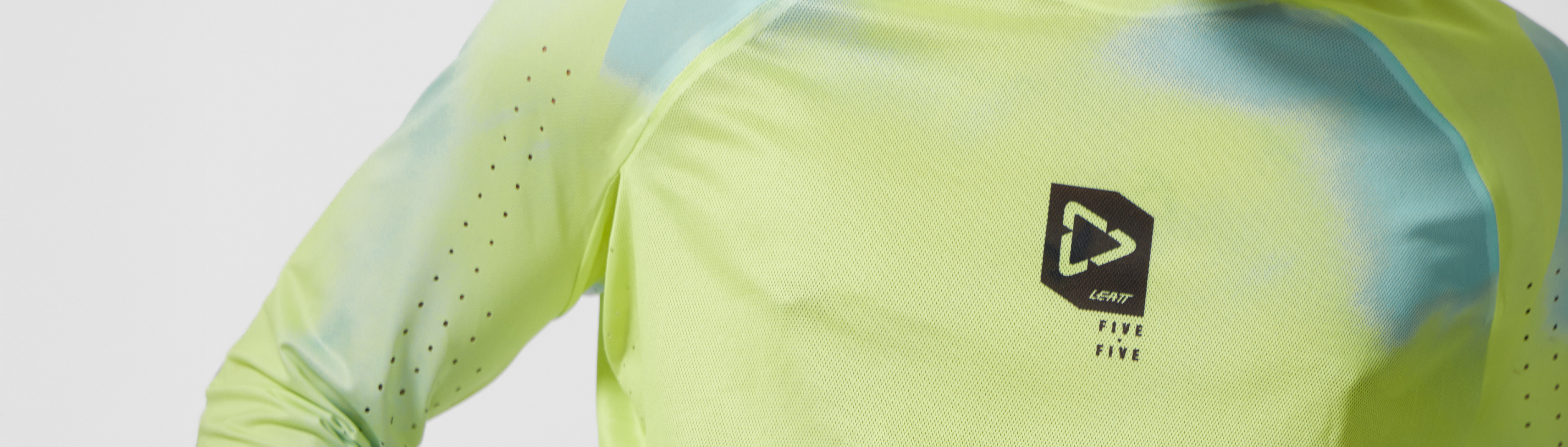 Close-up of a long-sleeve athletic top in bright neon yellow-green with a small black and white logo on the chest, shown against a clean white background.